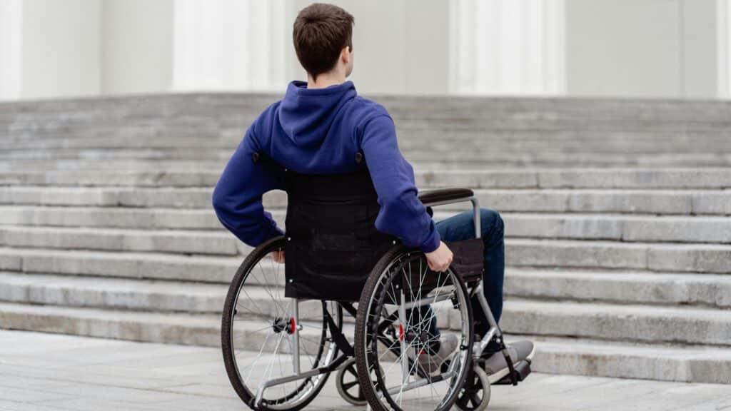 Oseba, ki uporablja invalidski voziček pred stopnicami.