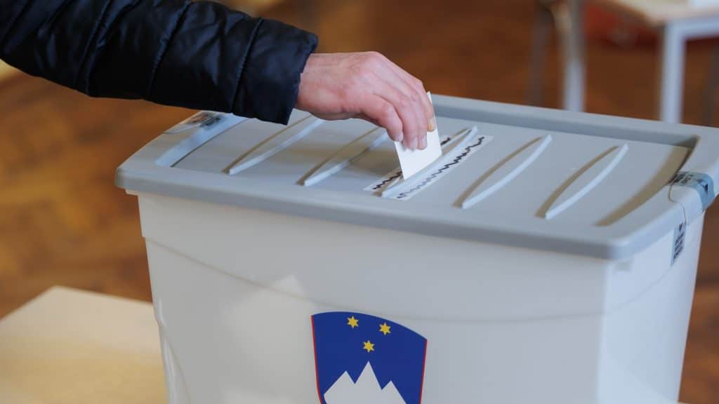 Na sliki volilna skrinjica in roka, ki vanjo vlaga volilni list.