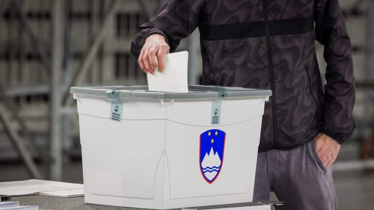 Oseba oddaja svoj glas na državnozborskih volitvah v volilno skrinjico.